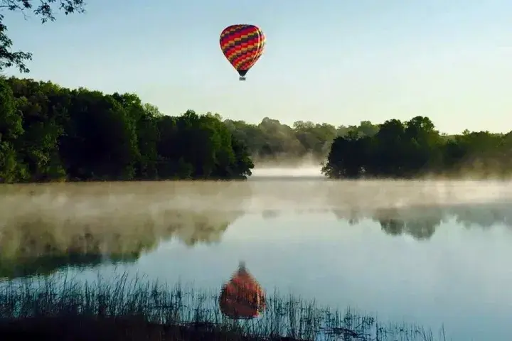 A Stillwater Balloons hot air balloon drifting over mist on the water at sunrise