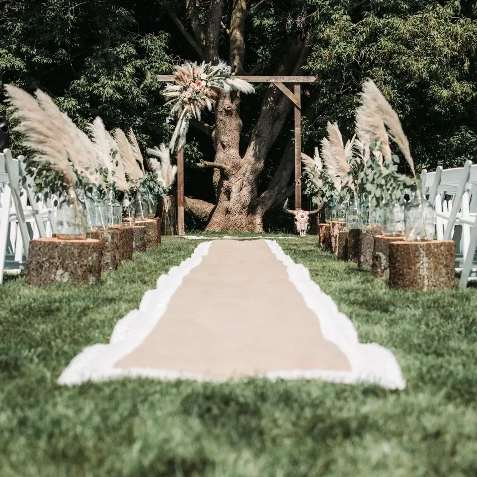 An outdoor ceremony aisle lined with pampas grass beneath a large oak